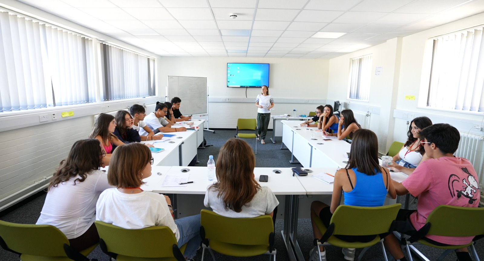 Teacher leading a classroom lecture with students seated in a U-shaped arrangement, fostering interaction and engagement.