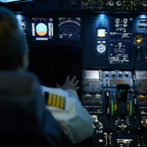 Rear view of unrecognizable pilot sitting at control panel with radar devices and flight system buttons and flying plane on autopilot